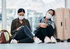 Shot of two young women wearing masks while waiting together in an airport